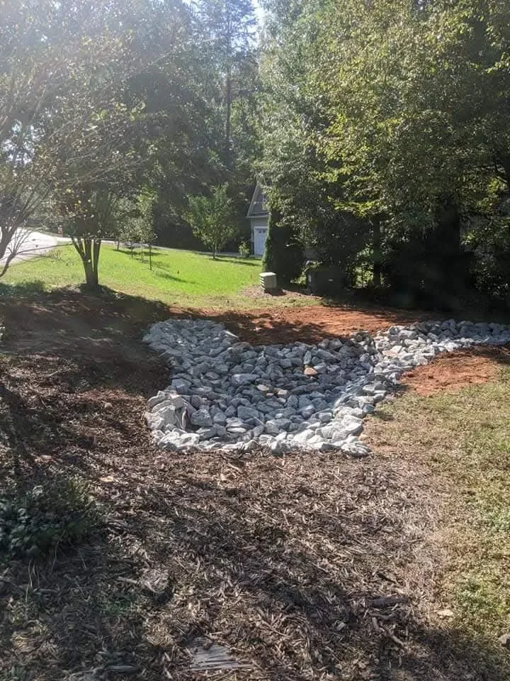 A stone-lined dry creek swale built to carry runoff away from a yard — Little Acres Grading