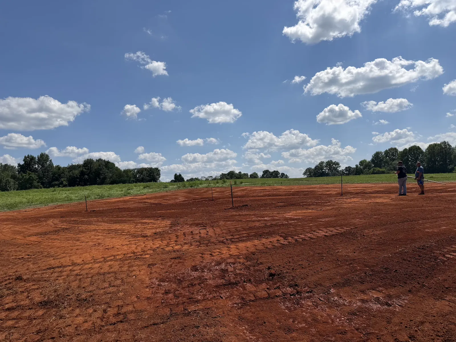 A house pad graded to elevation with corner stakes set for the builder — Little Acres Grading