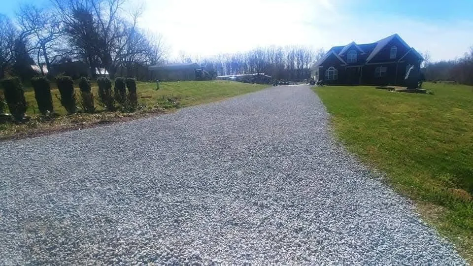 A gravel driveway curving up to a farmhouse under mature shade trees — Little Acres Grading
