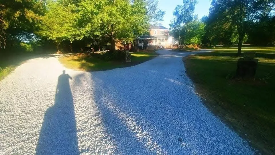 A freshly stoned driveway running along a shaded tree line — Little Acres Grading