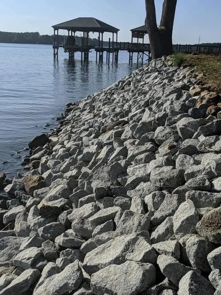 A stone shoreline armored with rip-rap beside a private boat dock — Little Acres Grading